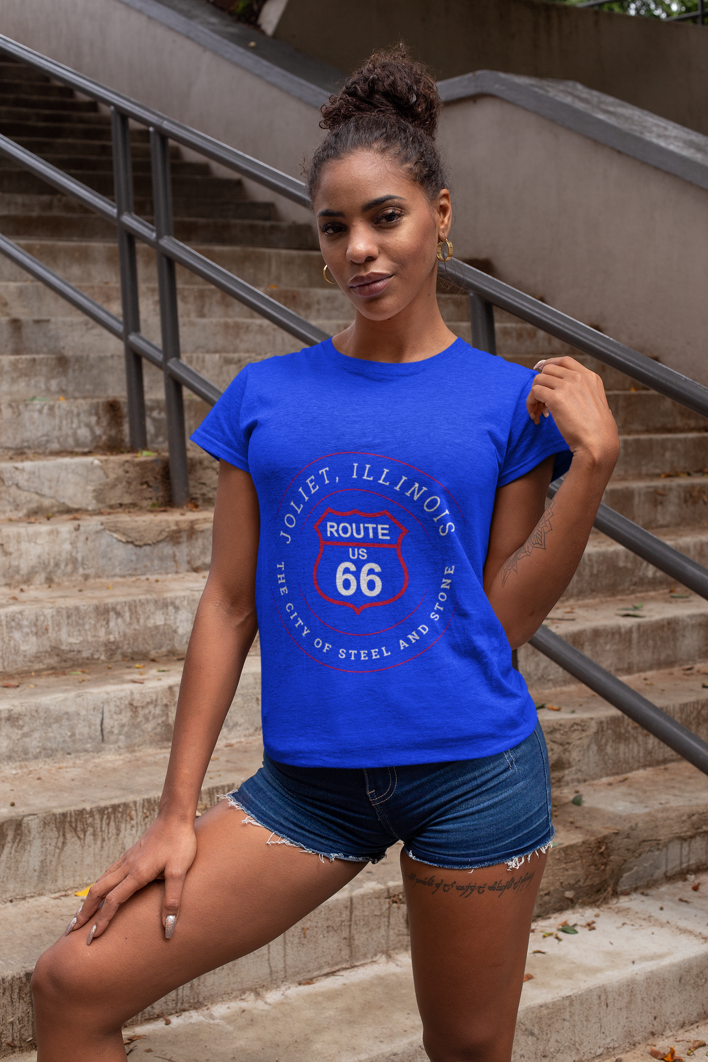 Smirking woman wearing a tri-blend vintage royal tee featuring a retro Route 66 Joliet IL "The City of Steel and Stone" graphic.