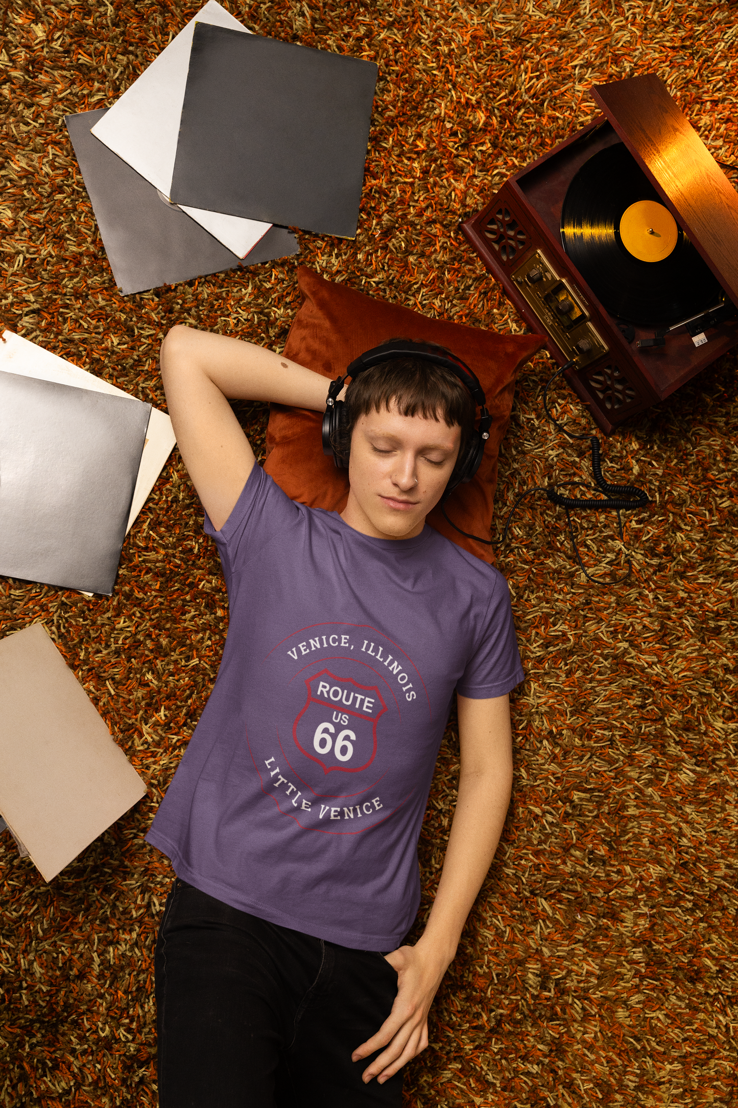 Male model wearing a heather team purple retro Route 66 unisex jersey tee with a Venice, IL:: "Little Venice" design while he lays on the carpet and listens to vinyl