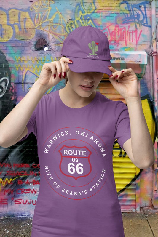 Female model wearing a heather team purple retro Route 66 unisex jersey tee with Warwick, OK "Site of Seaba's Station" design. She also has a heather team purple "The Heart of Route 66" tagline and a green cactus design