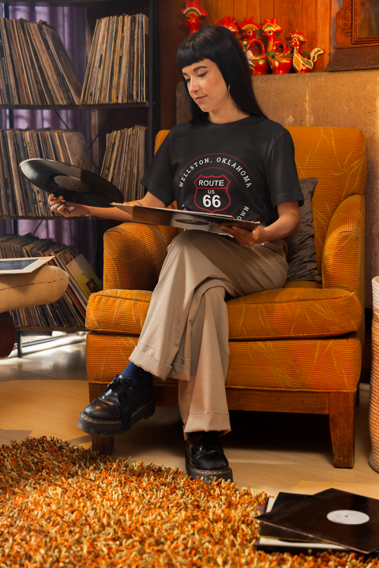 Female model wearing black heather retro Route 66 unisex jersey tee with Wellston, OK "Gap & Loop Town" design while checking out a vinyl record
