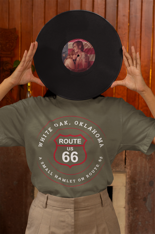Model holding a Lana Del Rey vinyl which is obstructing his face and wearing a heather military green retro Route 66 unisex jersey tee with White Oak, OK "A Small Hamlet on Route 66"  design