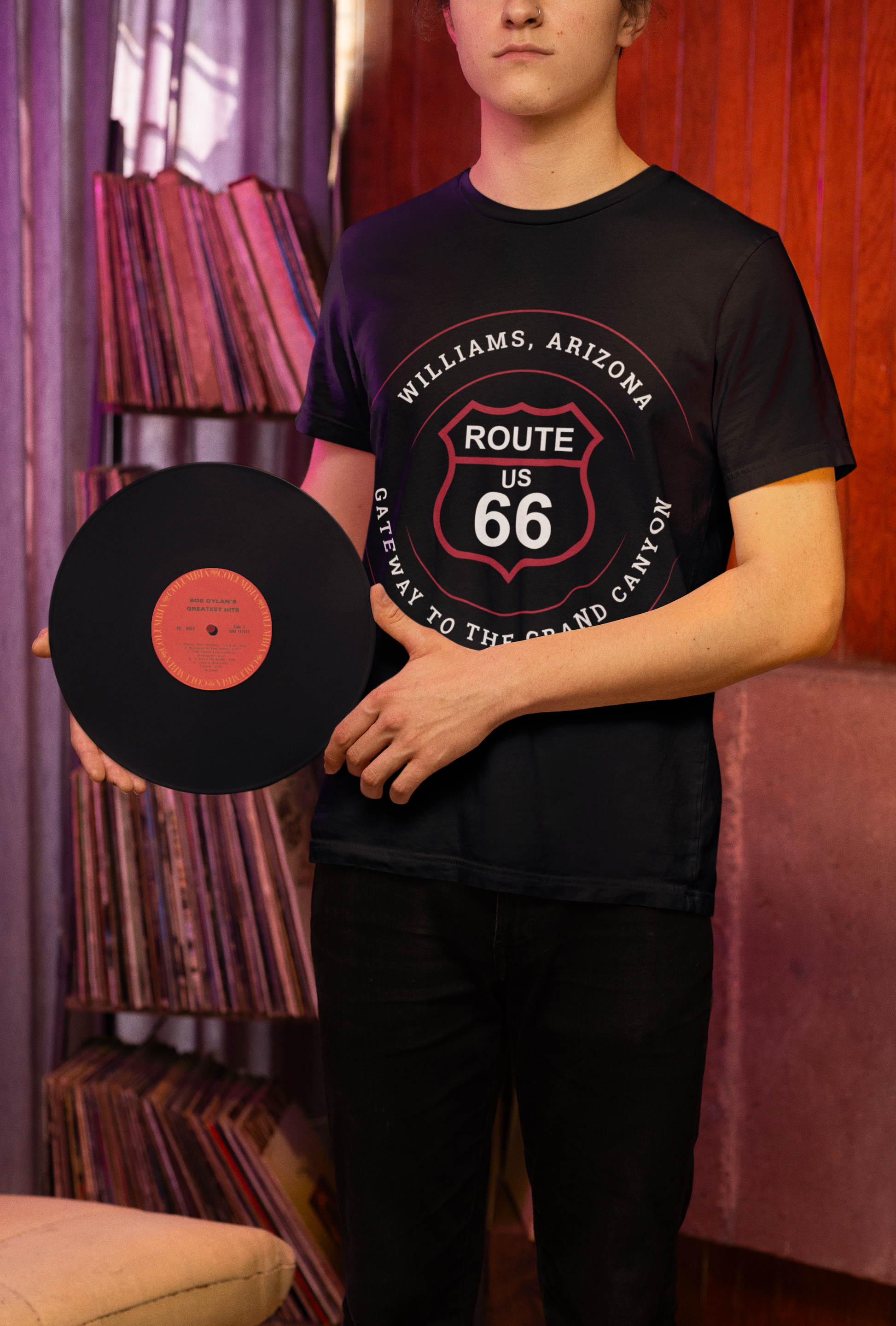 Male model holding a Bob Dylan vinyl and wearing a black retro Route 66 unisex jersey tee with Williams, AZ: "Gateway to the Grand Canyon" design