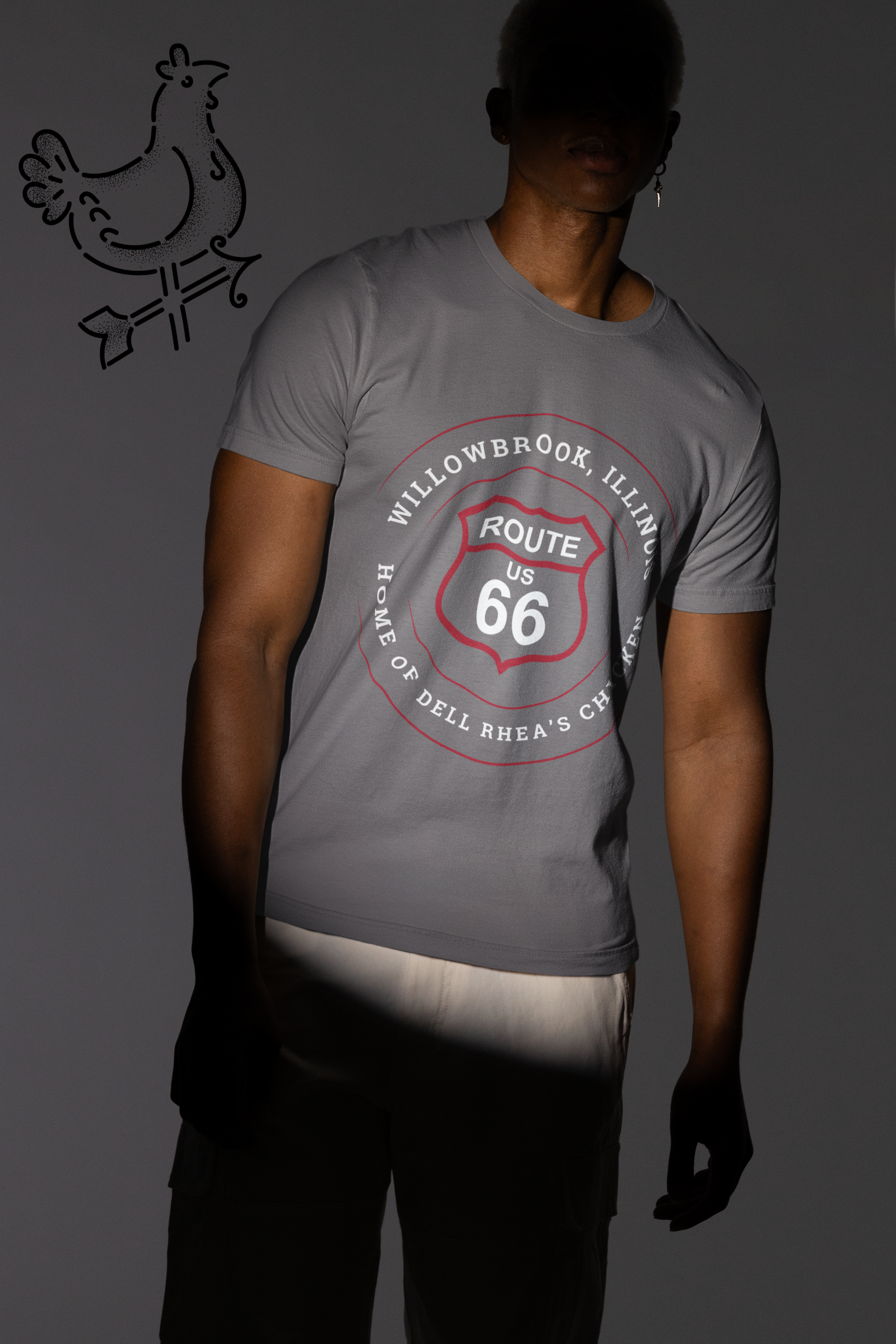 Male model wearing a grey retro Route 66 unisex jersey tee with a Willowbrook, IL: "Home of Dell Rhea's Chicken" design