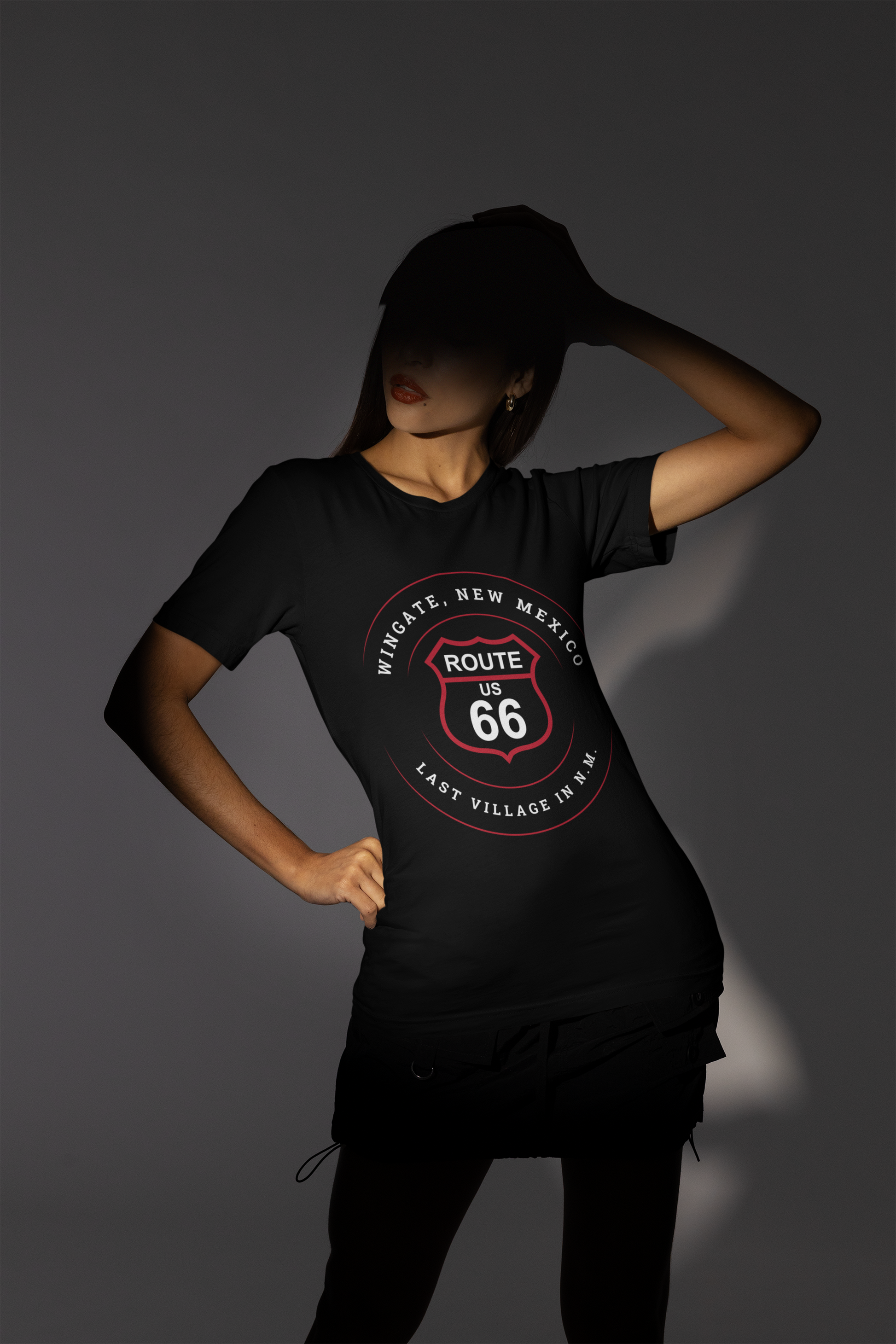 Female model wearing a black retro Route 66 unisex jersey tee with a Wingate, NM: "Last Village in N.M." design