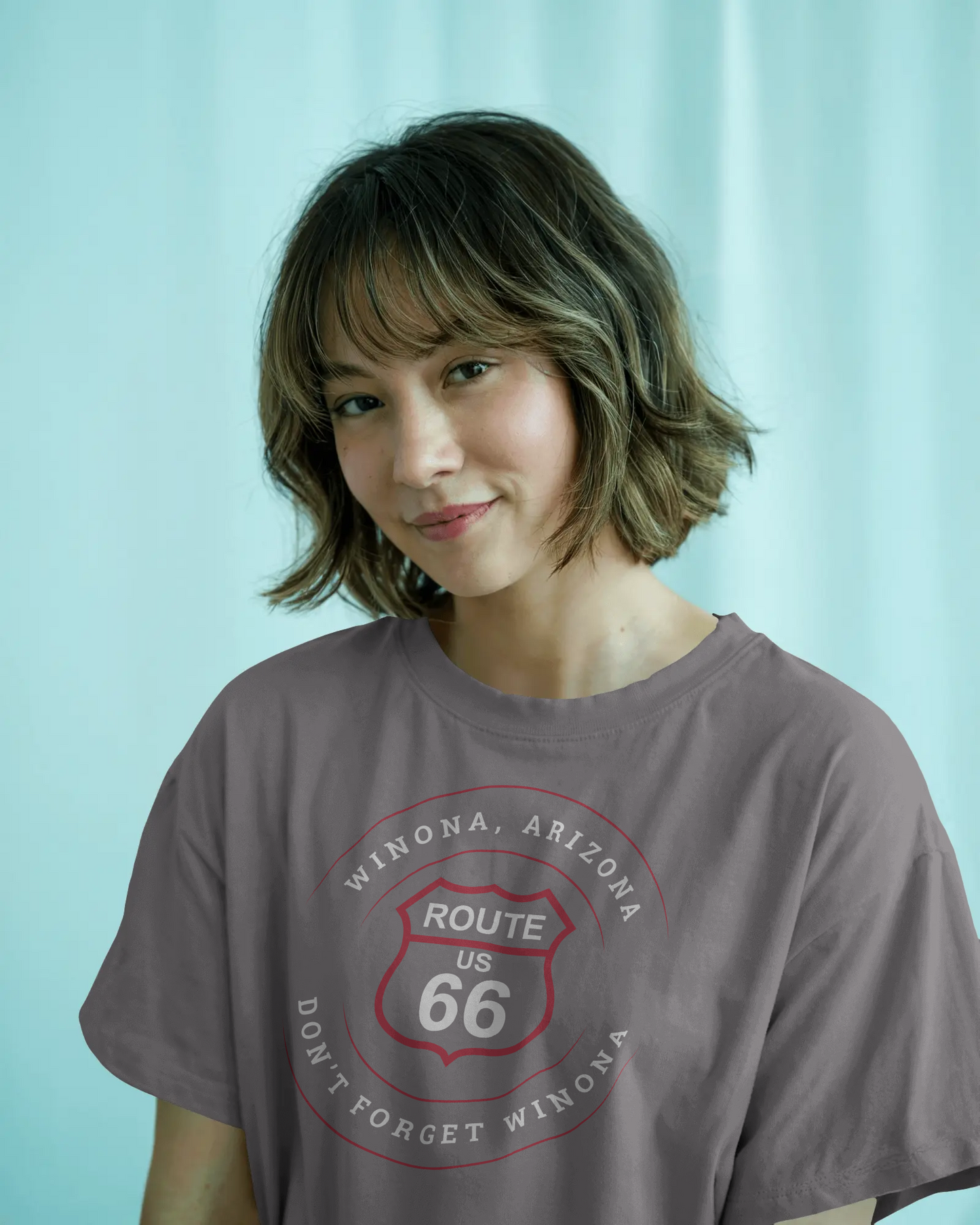 Female model wearing dark grey heather retro Route 66 unisex jersey tee with Winona, AZ: "Don't Forget Winona" design