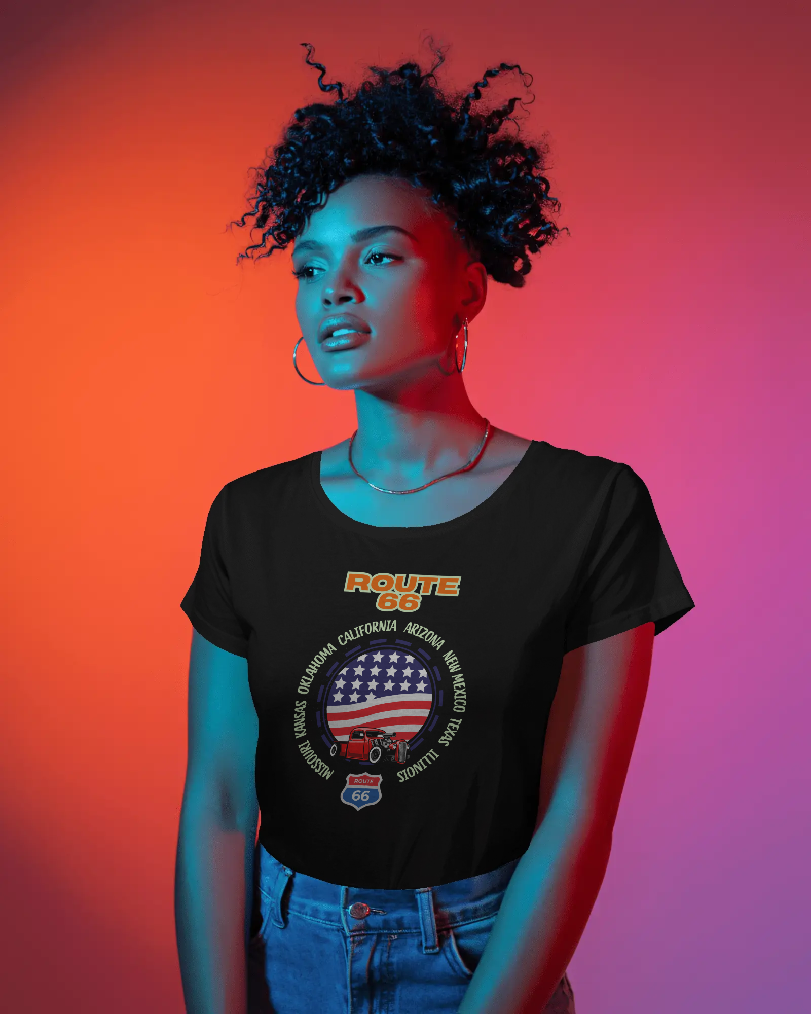 Woman wearing a black Route 66 t-shirt featuring a vintage car, a circular American flag design and the names of all eight Route 66 states, posing under red and blue lighting.